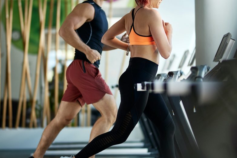 Athletic couple jogging on treadmills during sports training in a gym.